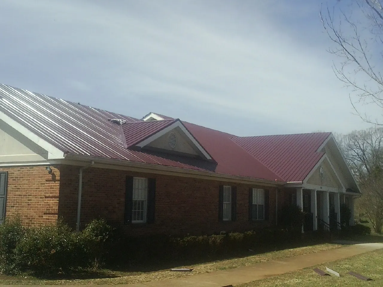 Red metal roof with gabled entries on a long brick building, from a Hail Damage Roof Repair job in Mantachie