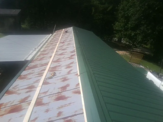 Old rusted panels beside newly installed green metal roofing — Wind Damage Roof Repair by Roofing Brothers in Mantachie