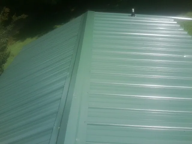 New green metal panels meeting at the ridge of a roof — Flat Roof Repair work by our crew in Mantachie