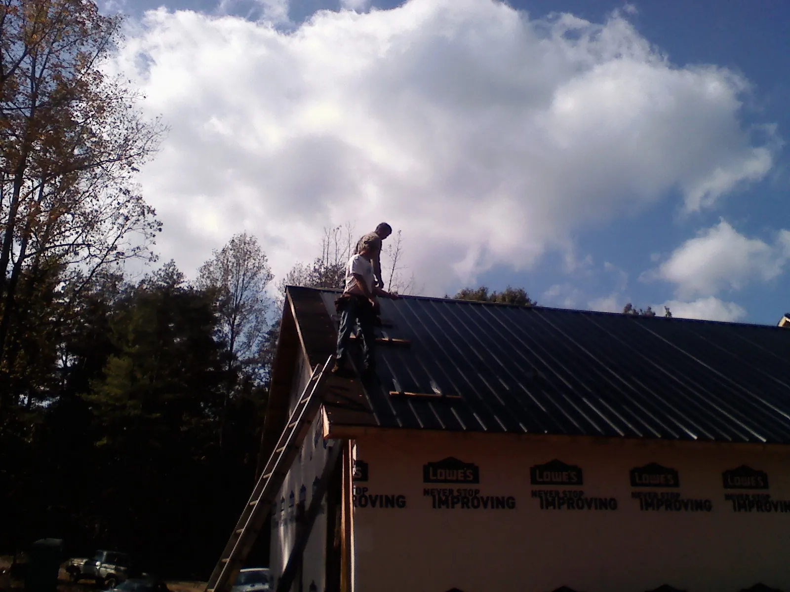 Roofer fastening dark metal panels high against a cloudy sky, from a Roof Inspection job in Mantachie