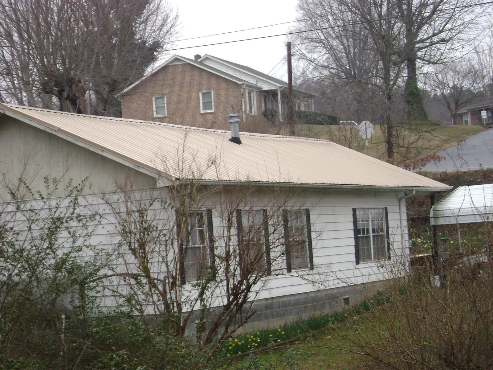 Tan metal roof on a white sided house set into a hillside — Commercial Roofing by Roofing Brothers in Mantachie