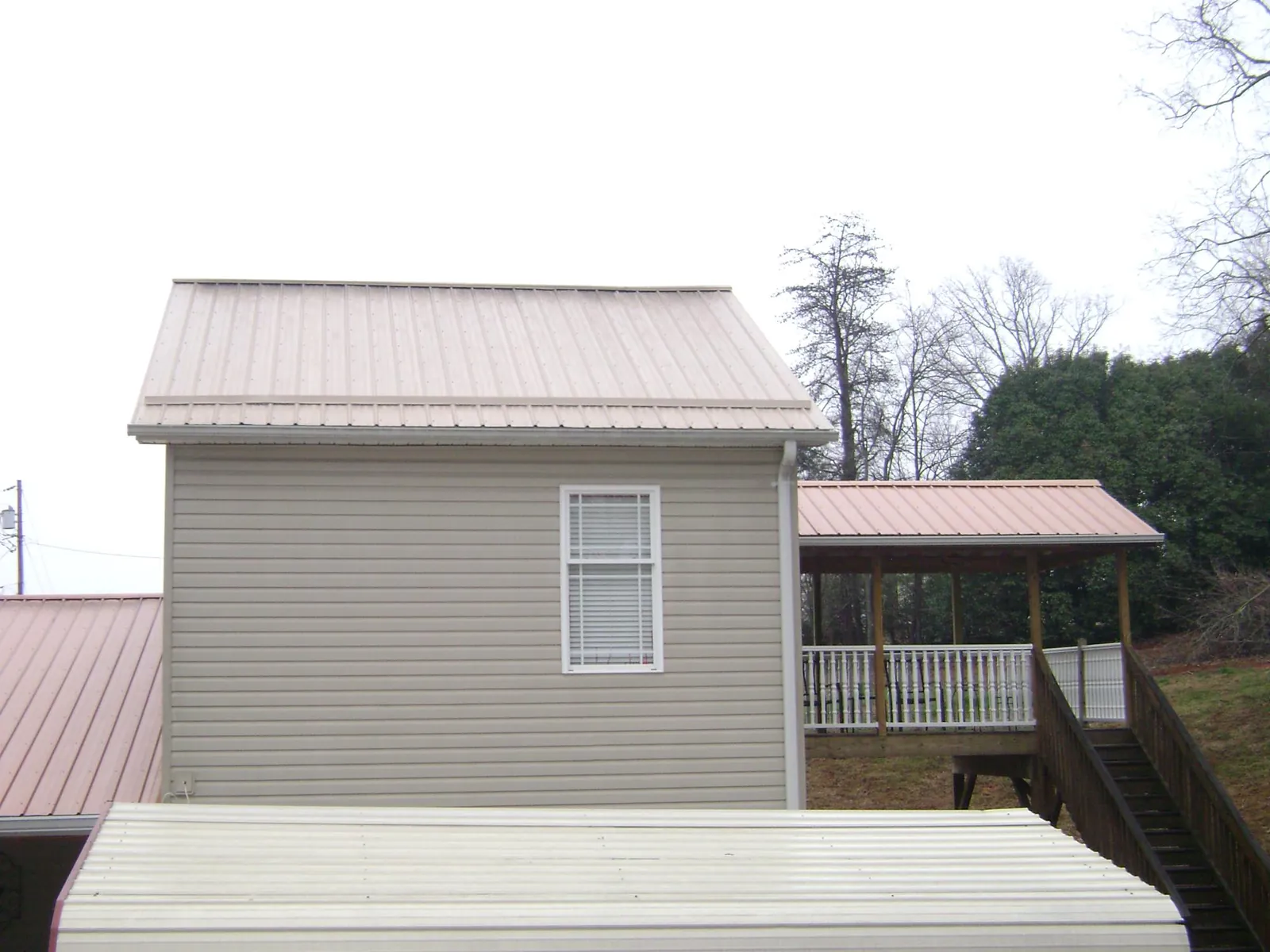 Tan metal roofs on a two story addition and attached porch, from a Roof Replacement job in Mantachie